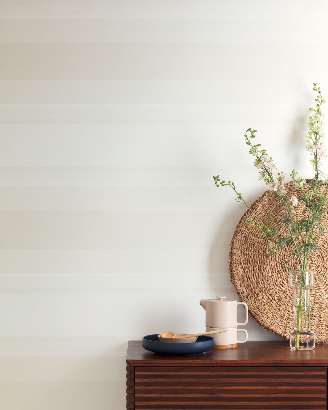 Ljus beige horisontell randig tapet med en försiktig nyansskillnad med sideboard fyllt av porslin och grön kvist