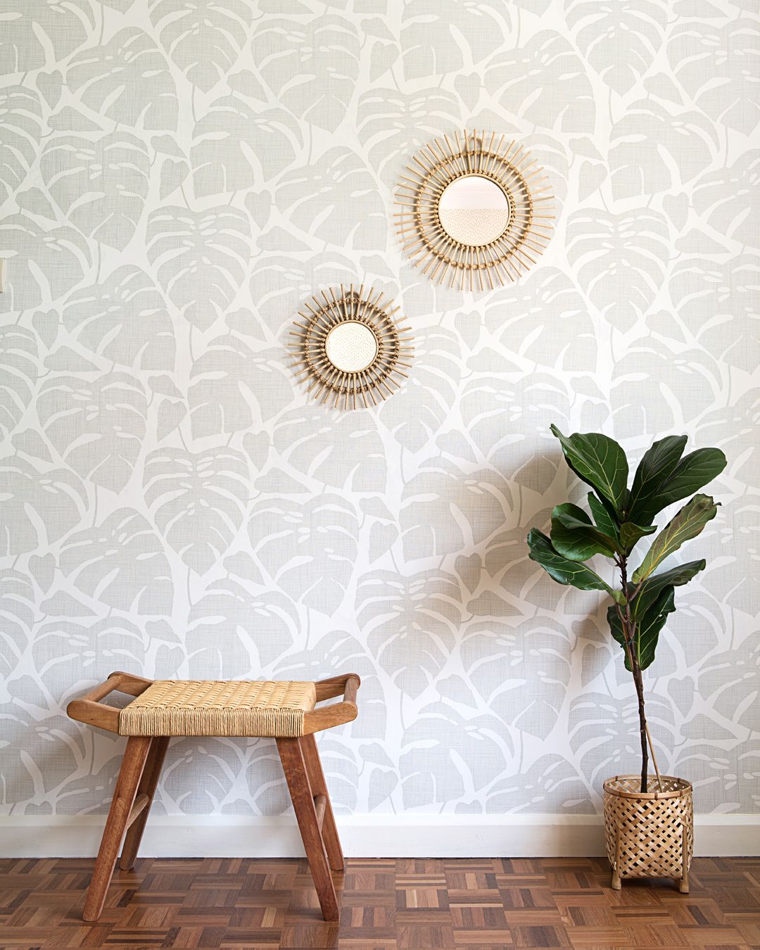 Ljus tapet med stora monsterablad i grått med trämöbler framför