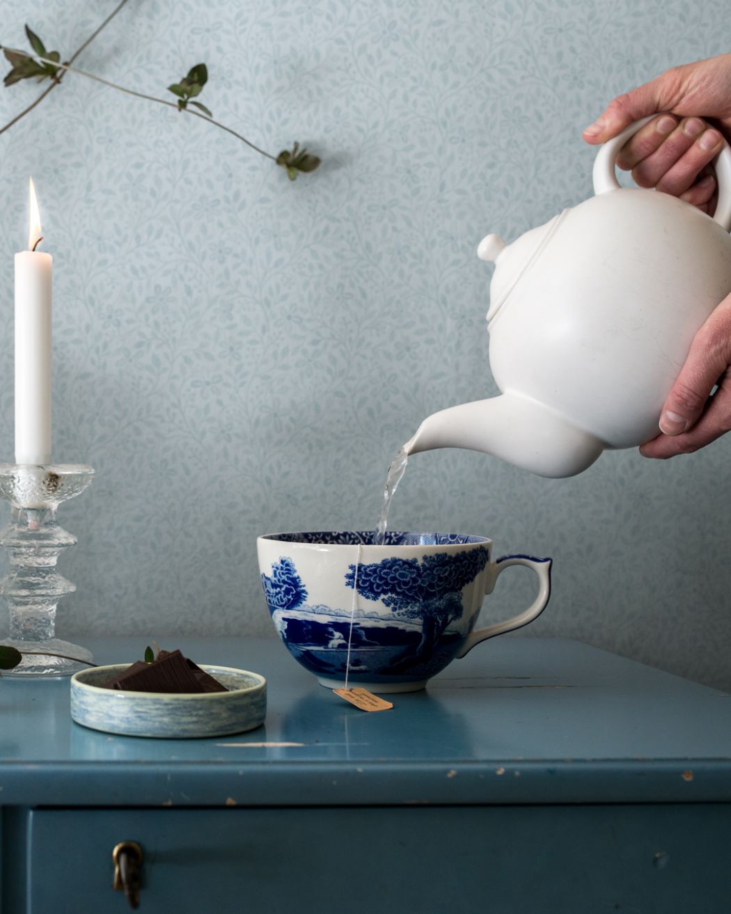 ljusblå småblommig tapet som går ton i ton. Blå byrå med blå kopp.