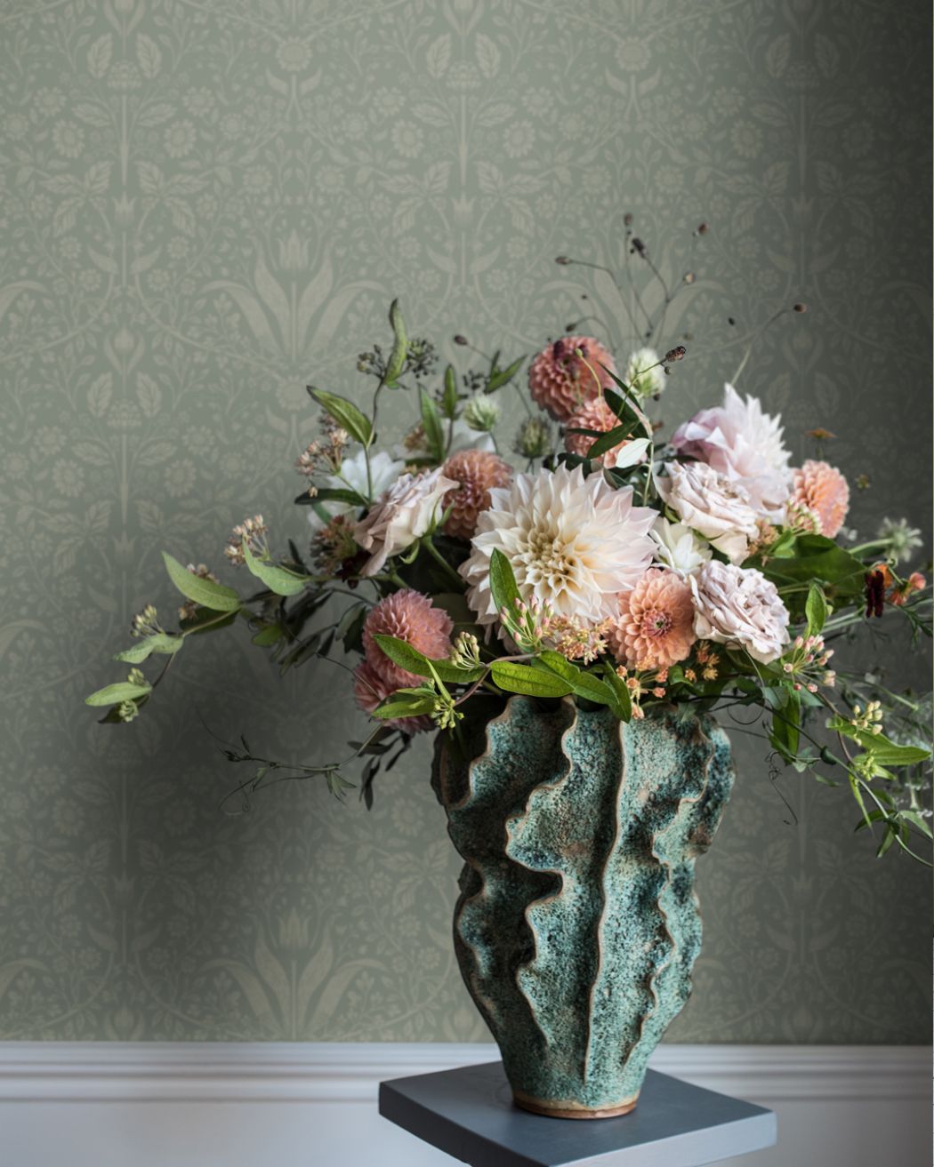 Ton i ton tapet med gröngrå botten och ljust gröna tulpaner bakom en grön vas med färgglada blommor